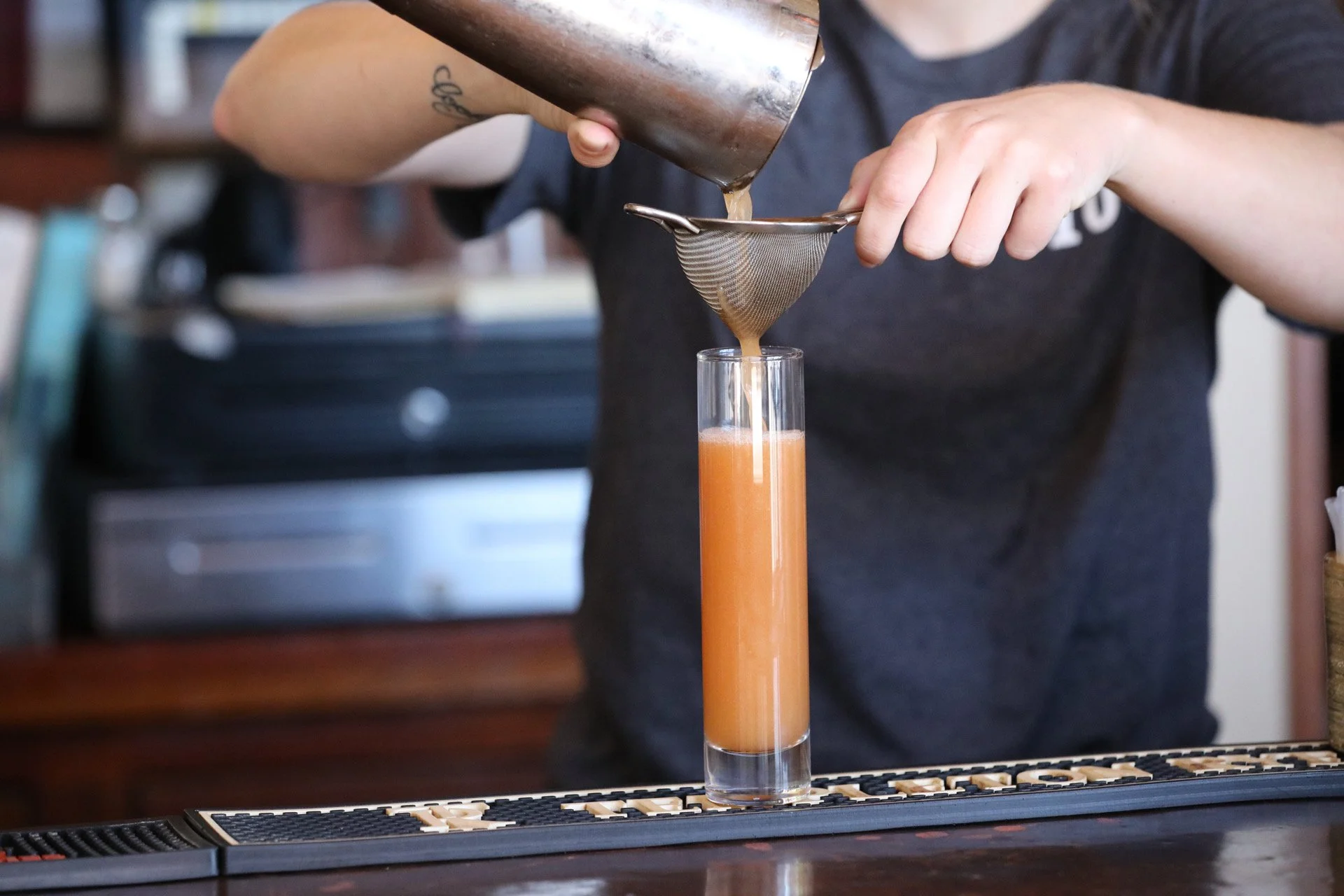 A bartender straining a cocktail into a tall glass